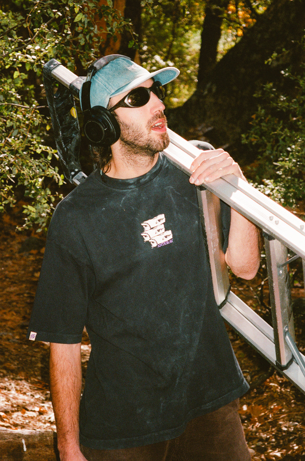 Man wearing headphones and sunglasses, holding a bike frame in a forest setting