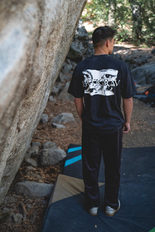 Person standing on a crash pad next to a rock face in a forest setting