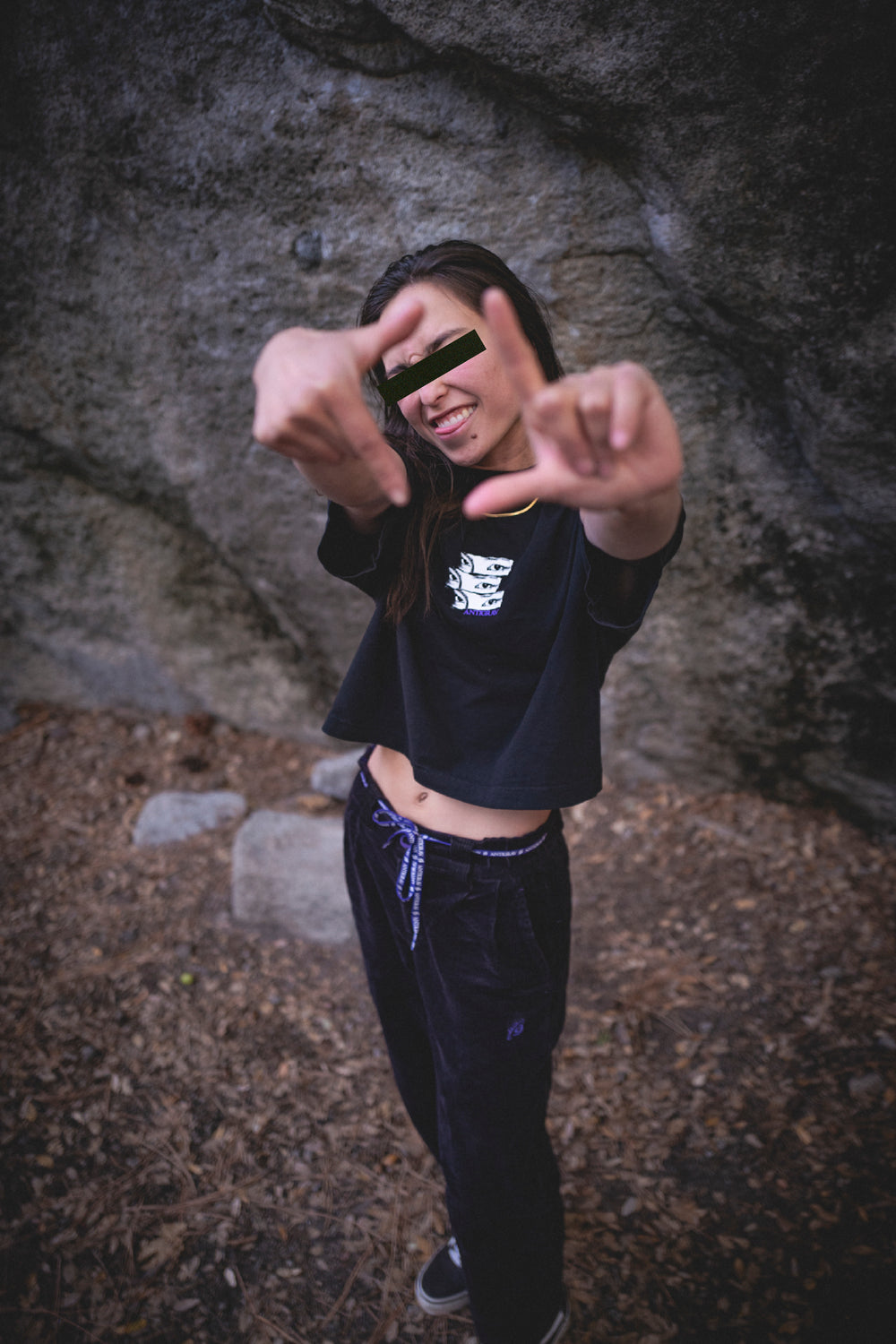 Person in black clothing making a peace sign gesture against a rocky background